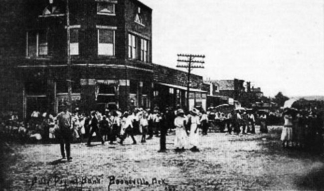 Three-story brick building and crowd on busy dirt road