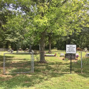 Gravestones and trees in cemetery inside chain link fence with sign outside it