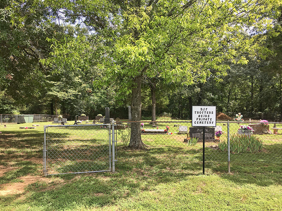 Gravestones and trees in cemetery inside chain link fence with sign outside it