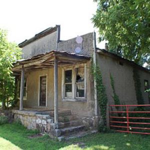 abandoned single-story building with small covered porch and red iron gate