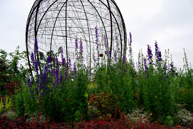 spherical latticed sculpture among purple flowers and various other plants