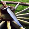 Large knife leaning on wooden wagon wheel in grass