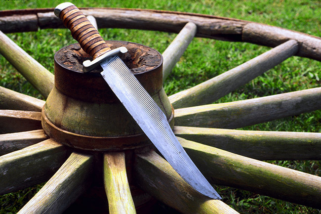 Large knife leaning on wooden wagon wheel in grass