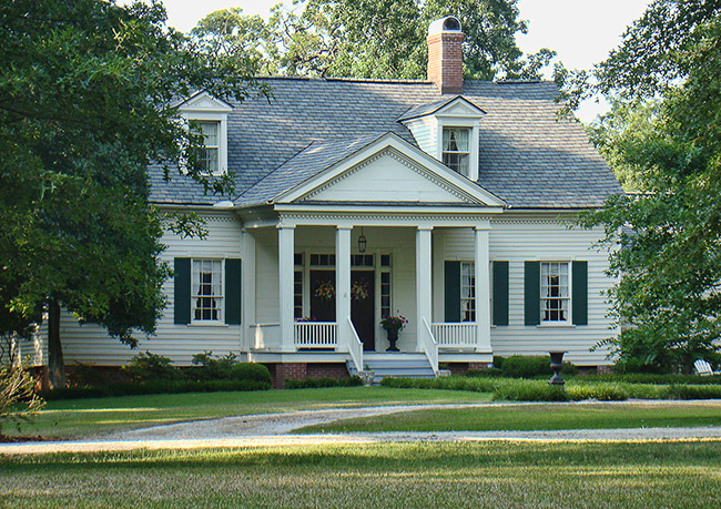 Two-story white house with dark shutters and four small columns on porch