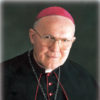 Old white man with glasses wearing a red cap and bishop's robes with crucifix necklace