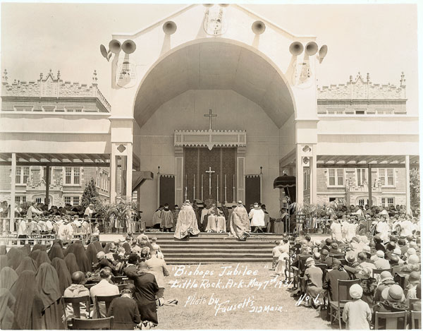 Crowd gathered outside at "Bishop's Jubilee" before exterior altar with stone building in the background