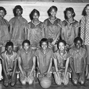 Group of young African-American girls in matching basketball uniforms and an African-American woman with glasses in dress