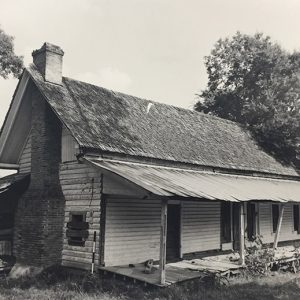 Abandoned dilapidated single-story house with covered porch and brick chimney