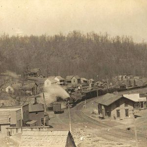 Steam locomotive passing through town on curved railroad with various houses and buildings