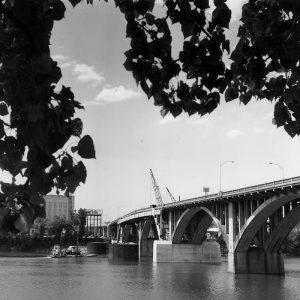 Concrete arch bridge over river during restoration with multistory buildings in the background
