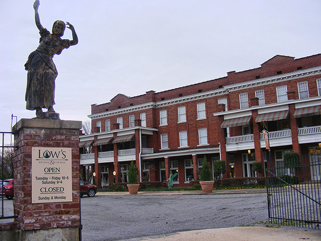 Statue of a dancing girl on brick column outside multistory brick building with parking lot