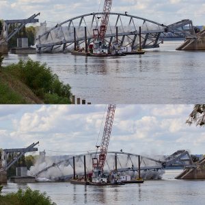 Steel arch bridge being torn down by crane barge on river