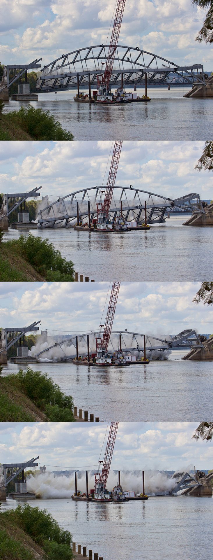 Steel arch bridge being torn down by crane barge on river