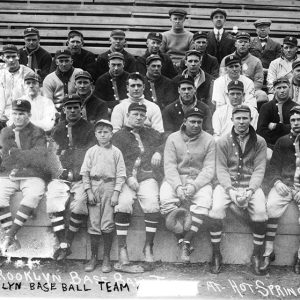 Group of white men in baseball uniforms with caps and jackets sitting on wooden bleachers
