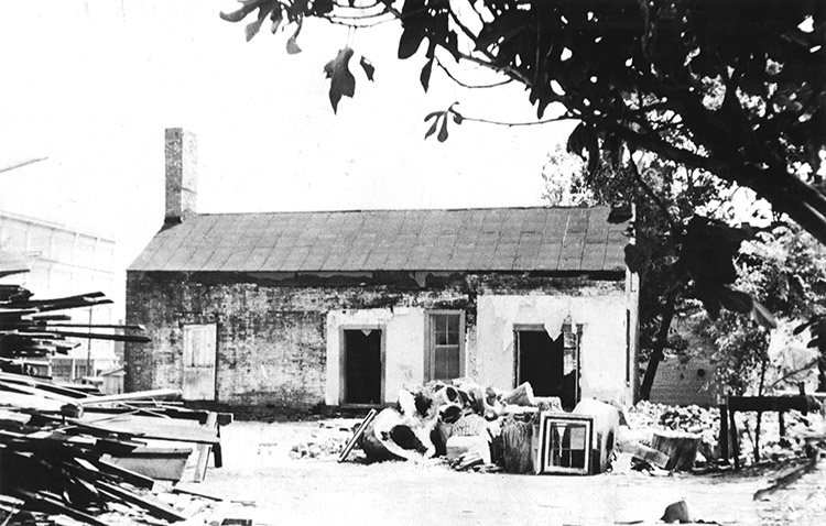 Dilapidated single-story house with debris piled in front yard