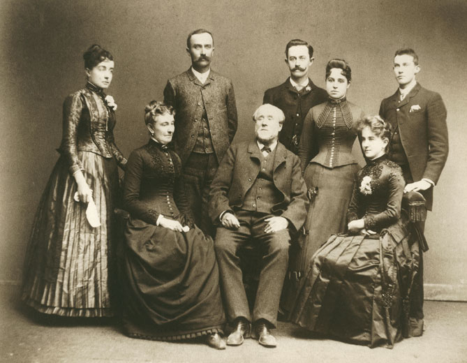 Older white men and women in formal clothes pose with their adult children for family portrait