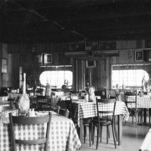 Tables with checkered tablecloths and chairs inside restaurant with items on shelves on the walls