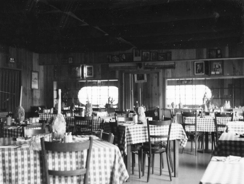 Tables with checkered tablecloths and chairs inside restaurant with items on shelves on the walls