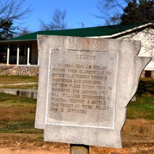 Engraved stone sign shaped like the state of Arkansas with building behind it