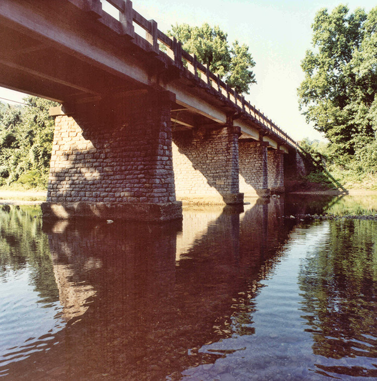 Underside of concrete bridge with stone columns over river
