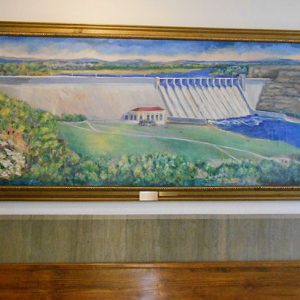 framed painting on wall showing a concrete dam with river and surrounding countryside