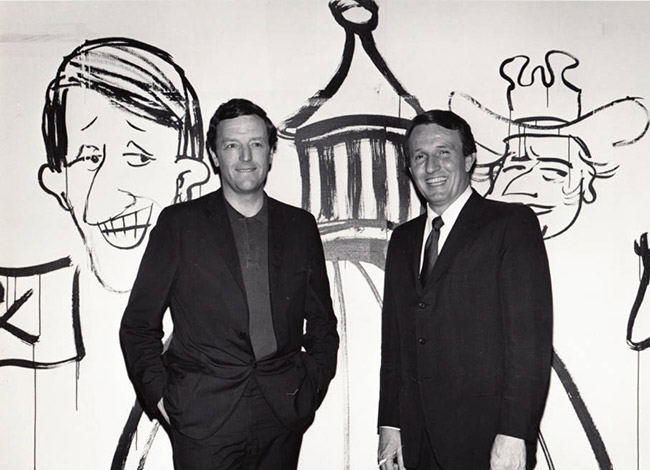 Two white men in suits smiling with caricatures on the wall behind them