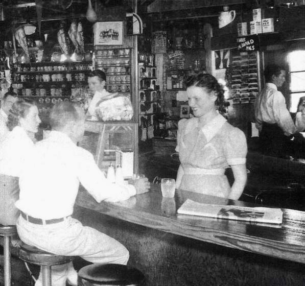 White woman in uniform serving white man and woman at bar