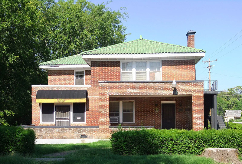 Front view of multistory brick house with covered porch and balcony with staircase