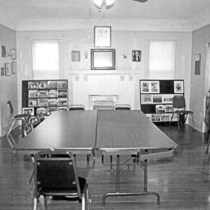 Interior of room with tables in its center and framed photographs on the wall in the background
