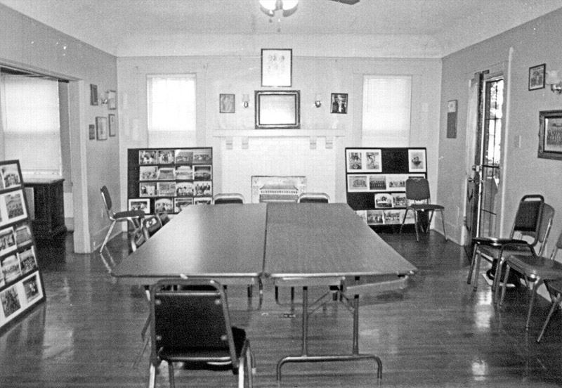 Interior of room with tables in its center and framed photographs on the wall in the background