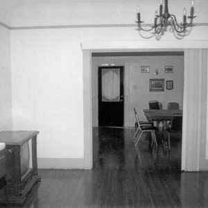 Interior of room with table and television on wood floors looking into another room with table and chairs in it