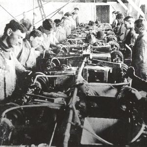 White workers sitting in two rows at machines in factory