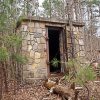 Small stone building in forest with open metal door