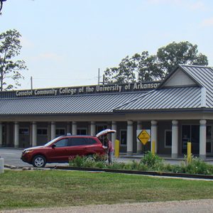 Single-story building with columns and covered walkways and parking lot with sign saying "Cossatot Community College of the University of Arkansas"