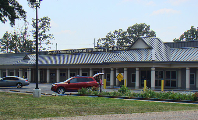 Single-story building with columns and covered walkways and parking lot with sign saying "Cossatot Community College of the University of Arkansas"