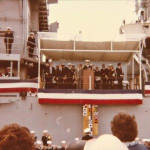 Group of officers and politicians speaking from balcony on naval vessel with red white and blue banners