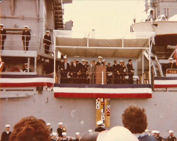 Group of officers and politicians speaking from balcony on naval vessel with red white and blue banners