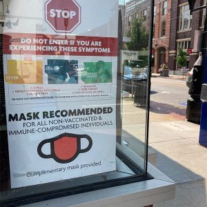 "Mask recommended sign" in building window with multistory building across the street in the background