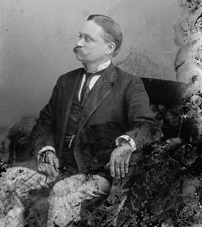 Profile of white man with mustache sitting in suit and tie