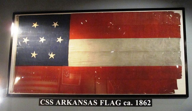 Red white and blue flag with three stripes and seven stars under glass