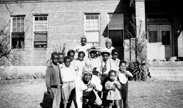 small group of African American students of various ages outside brick building