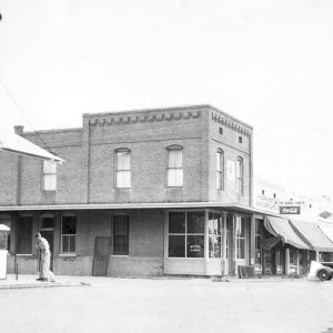 Street with multistory brick buildings with a car parked in front of the first-floor awnings and a white man sweeping on the corner
