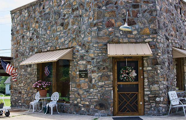 Single-story stone building with awnings over the door and windows with outdoor tables and chairs