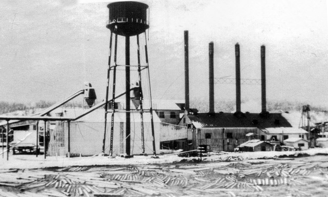 Lumber mill building with four smoke stacks and water tower