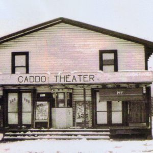 Symmetrical two-story building with porch with "Caddo Theater" written above the entrance