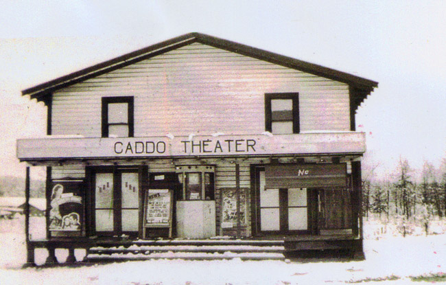Symmetrical two-story building with porch with "Caddo Theater" written above the entrance