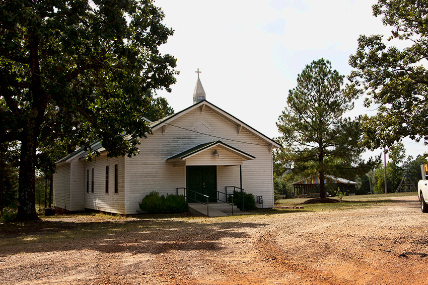 Single-story church building with covered entrance steeple and pavilion in the background
