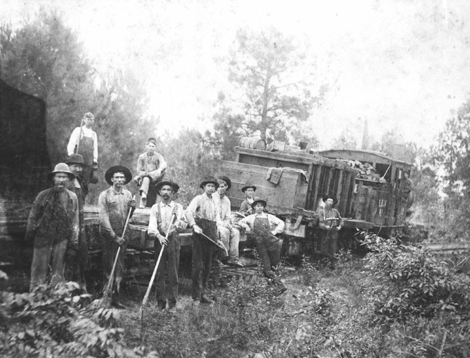 Group of white men, many in overalls, posing with a train while at work