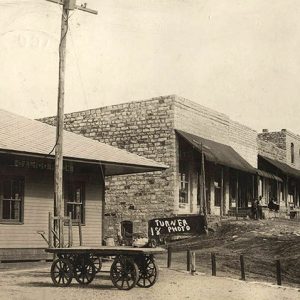 Train depot building with cart next to row of brick storefronts on dirt street