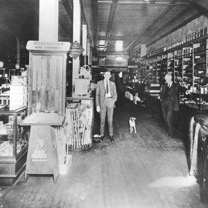 Two white men in suit and tie and small dog in hardware store